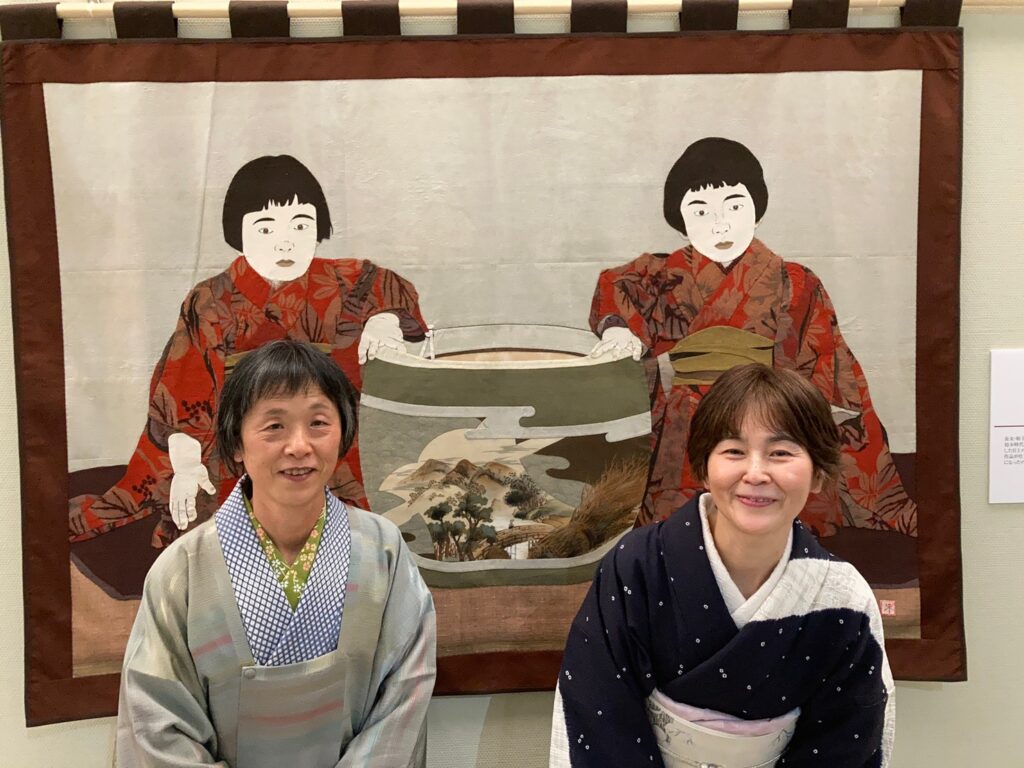 皆川未子「布絵の世界展」にて、絵と同じポーズをして記念写真。おしゃれな古布を使用された絵に思わずみとれてしまいました。